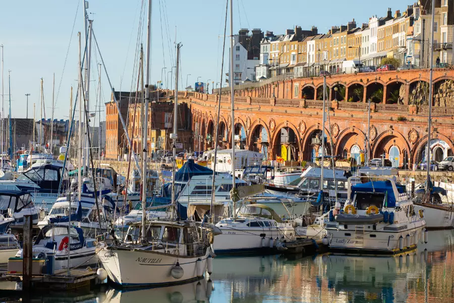 Looking through blue and white yachts and boats towards the brick built arches at the back of the harbour with the road above